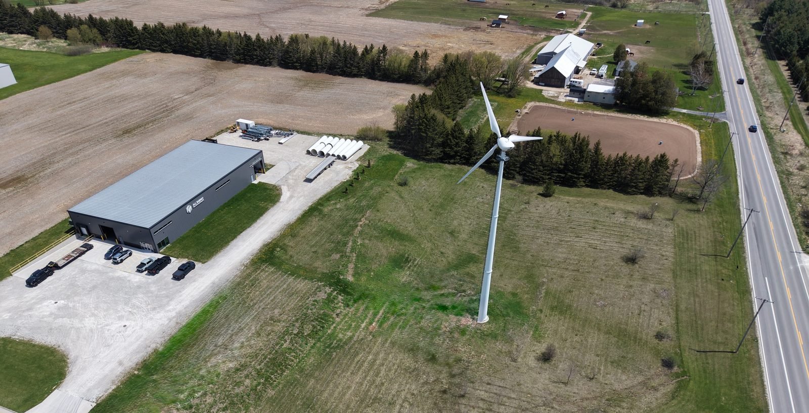 Aerial view of the All Energy Management facility in Two Rivers, Wisconsin, with warehouse, yard storage, and an on-site wind turbine
