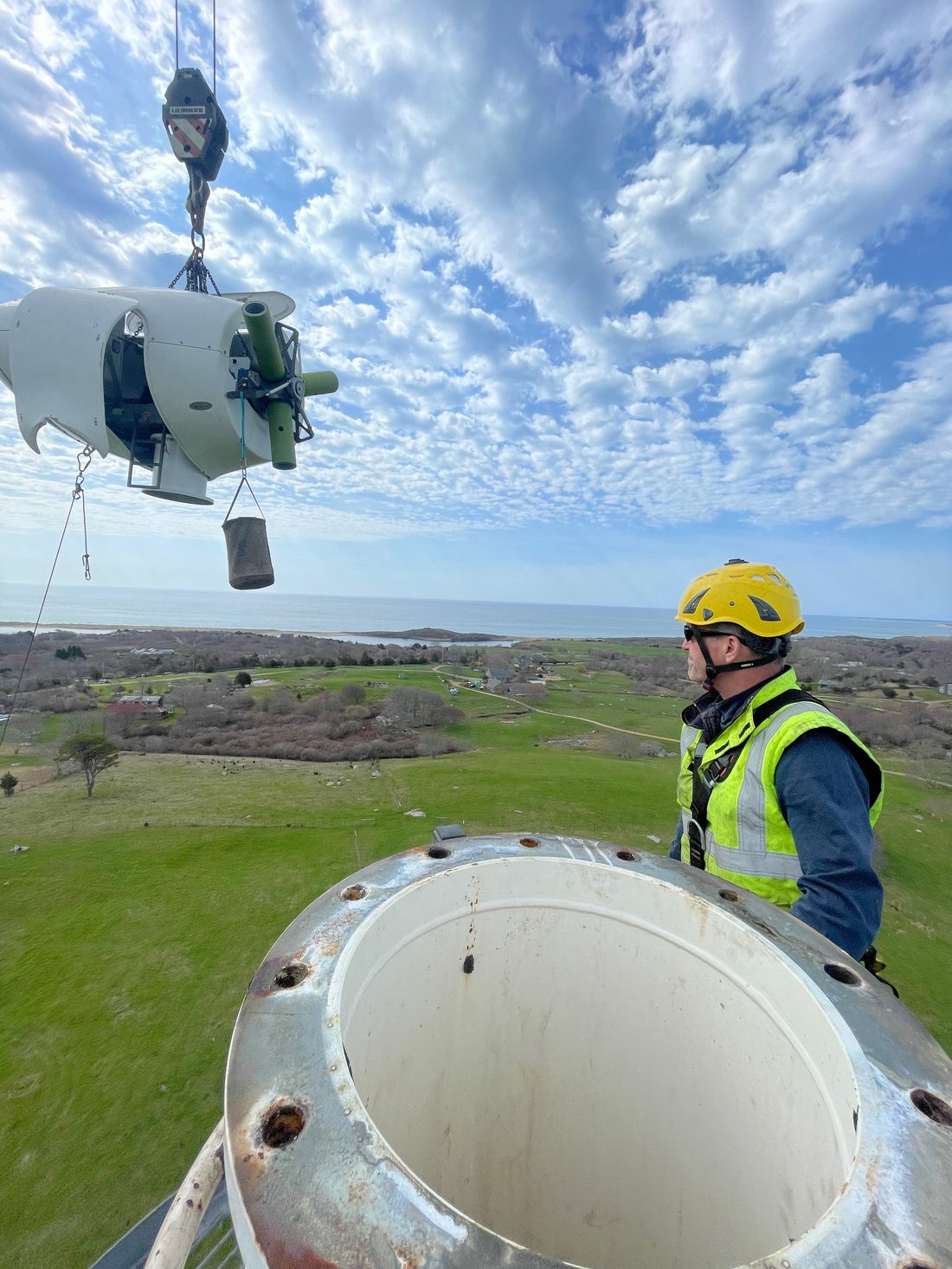 An AEM wind technician in safety harness and hi-vis gear working at the top of a turbine tower